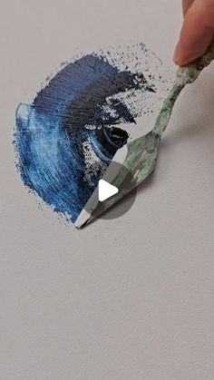 someone is painting something with blue and green colors on the paper while holding a paintbrush