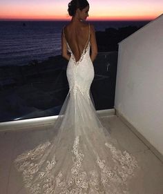 a woman in a wedding dress looking out over the ocean at sunset with her back to the camera