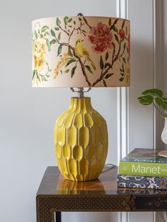 a yellow vase sitting on top of a wooden table next to a lamp and book