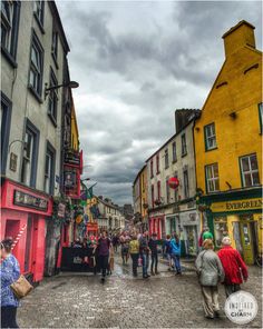 people are walking around in an old european town with colorful buildings and cobblestone streets