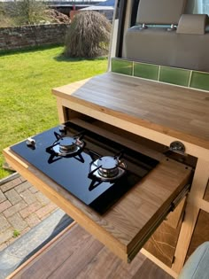 a stove top sitting on top of a wooden table next to a window with grass in the background