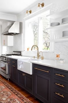 a kitchen with black cabinets and white counter tops, gold pulls on the faucets