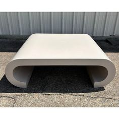 a white bench sitting in front of a metal wall on top of a cement floor