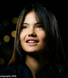 a close up of a person wearing a black shirt and smiling at the camera with lights in the background