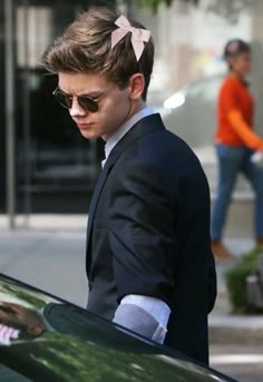 a young man in a suit and sunglasses is getting out of a car with his hand on the door handle