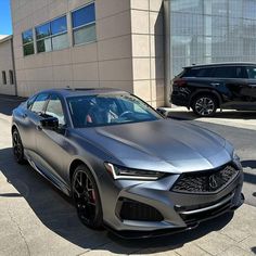 a silver acura is parked in front of a building with other cars on the street