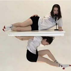 a woman laying on top of a white table next to another woman in black shorts