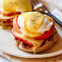 two eggs benedicts with tomatoes and cheese on a white plate next to a fork