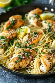 a skillet filled with pasta and shrimp topped with parmesan cheese, lemon wedges and parsley