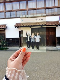 a person holding up an old photo in front of a building with doors and windows