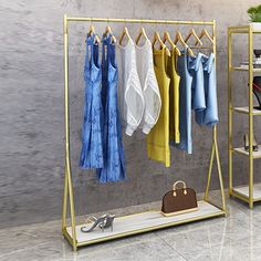 clothes hanging on racks in front of a wall with shoes and handbags next to it