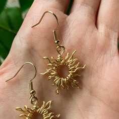 a pair of gold sun earrings sitting on top of a hand