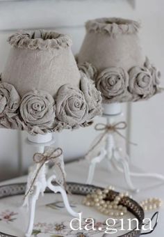 two lamps with roses on them sitting on a table next to a mirror and beaded bracelet