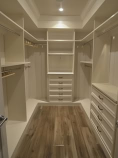 an empty walk in closet with wooden flooring and white cabinets, lights on the ceiling