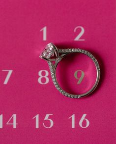 a diamond ring sitting on top of a pink surface next to a clock with numbers