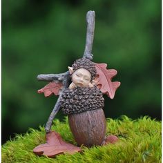 a small figurine sitting on top of a moss covered ground with an acorn