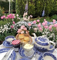 blue and white china set up on a table with flowers in the background