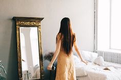 a woman standing in front of a mirror next to a bed