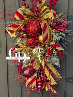 a red and gold christmas wreath hanging on the side of a wooden fence with ornaments