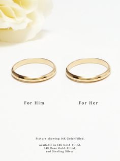 two gold wedding rings sitting on top of a white table next to a flower and the words for him or her