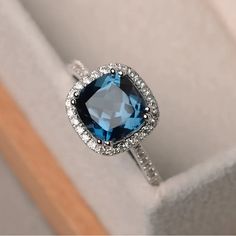 an engagement ring with a blue topaz surrounded by white diamonds in a gift box