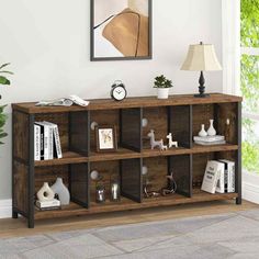 a wooden shelf with books and pictures on it in front of a window next to a lamp