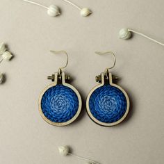 a pair of blue and white woven earrings on top of a gray surface with flowers in the background