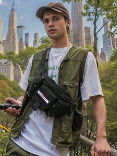 a young man wearing a hat and carrying a camera in his back pack while standing next to a fence