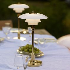 the table is set with wine glasses and plates of grapes on it, along with two lamps