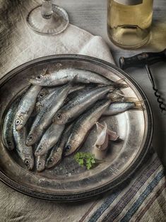 there are many small fish on the plate next to some wine glasses and a bottle