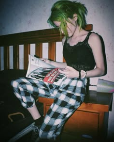 a woman with green hair sitting on a bed reading a magazine and looking at her phone