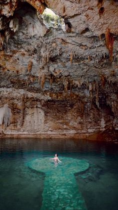 a person swimming in the water near a cave with stalate formations on it