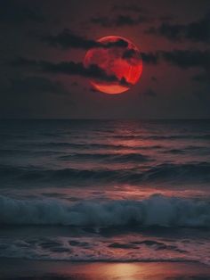 the moon is setting over the ocean with waves in front of it and red light reflecting on the water