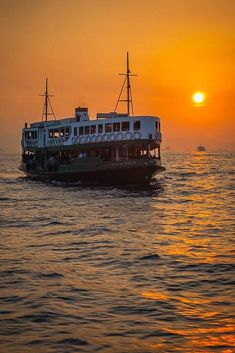 a large boat floating on top of the ocean at sunset with people sitting on it