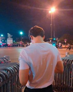 a man standing next to a fence looking at the street in front of him on a dark night