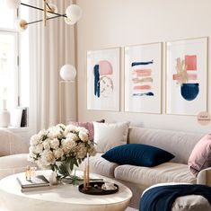 a living room filled with white furniture and paintings on the wall above it's coffee table