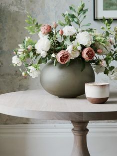 an arrangement of flowers in a large vase on a table with a cup next to it