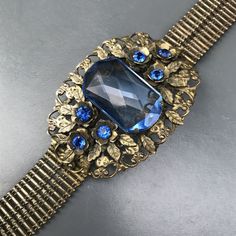 WIDE Vintage Art deco bracelet ~ with beautiful details with central large ,open-back faceted sapphire cab prong set on an gold tone openwork metal base ~ Embossed side link belt ~ Bracelet ends with hidden tongue and box clasp Dates 1930's - 1940 Measures : bracelet is 7 inches in wearable length x 1 3/4 inches max width . Condition : bracelet is in good old condition ~ Can see wear to gold gilding ,underneath silverish metal can be seen at places ~ Can see a small repair mark on the backside ( Victorian Jeweled Bracelets For Formal Occasions, Formal Jeweled Metal Bracelets, Formal Jeweled Bracelet Jewelry, Formal Jeweled Bracelet, Formal Costume Jewelry Bracelet With Jewels, Antique Jeweled Jewelry For Formal Occasions, Antique Jeweled Bracelet For Formal Occasions, Antique Formal Jewelry, Art Deco Evening Jewelry With Jewels