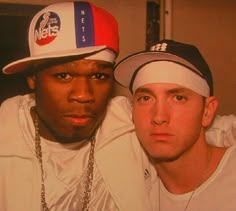 two young men are posing for the camera with one wearing a hat and the other in a white jacket