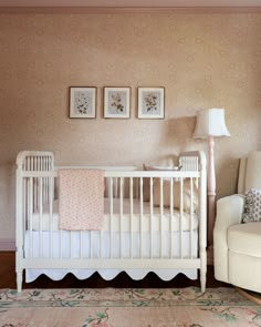 a white crib in the corner of a room with two pictures on the wall