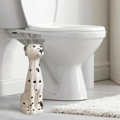 a white toilet with a dalmatian figurine sitting on the floor next to it