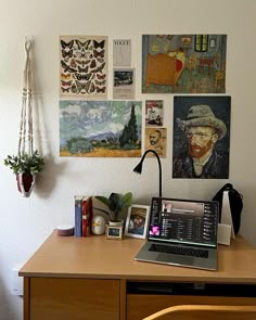 a laptop computer sitting on top of a wooden desk next to a wall covered in pictures