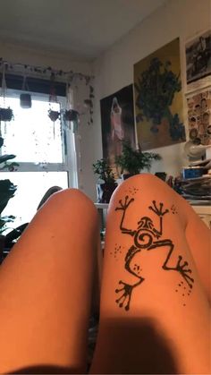 someone has drawn a frog on their leg and it looks like they are sitting in the living room