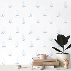 two books and a potted plant sit on a table in front of a wallpaper with sailboats