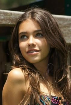 a beautiful young woman standing next to a wooden fence with her hair blowing in the wind