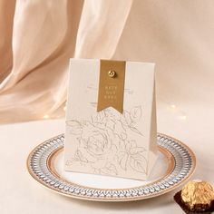 a white and gold plate with a card on it next to a piece of chocolate