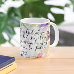 a coffee mug sitting on top of a wooden table next to a book and plant