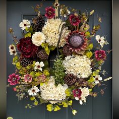 a wreath with flowers and pine cones hanging on a door