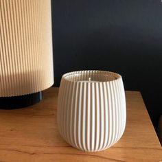 a white vase sitting on top of a wooden table next to a black lamp shade