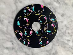 a black donut with multicolored bubbles on it sitting on a marble surface